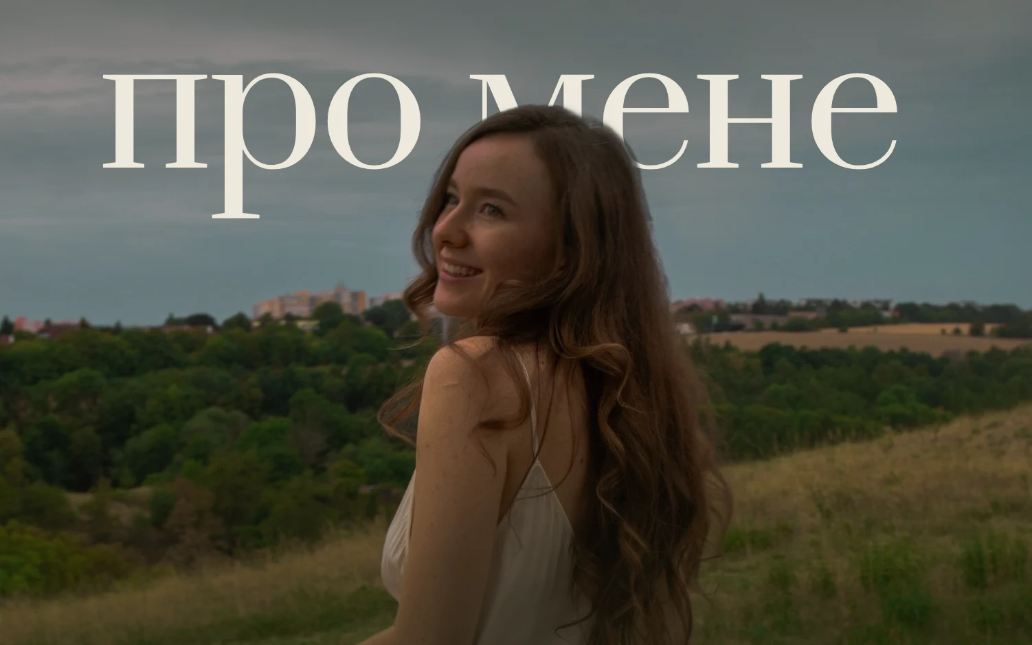 Аня озирається через плече й усміхається, за нею поле і пагорби